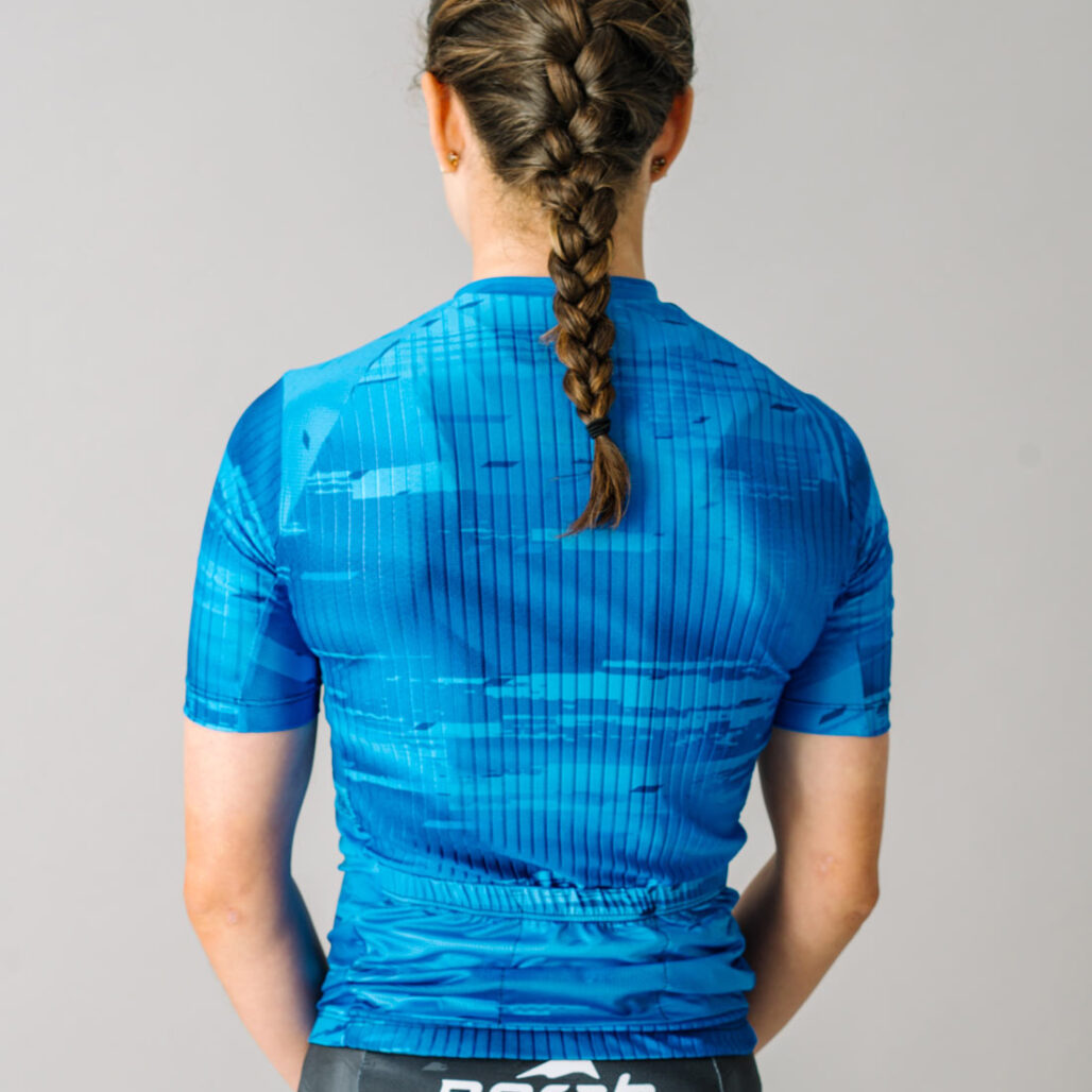 Back view of a female model wearing a blue custom Women's OTW Spark Cycling Jersey.
