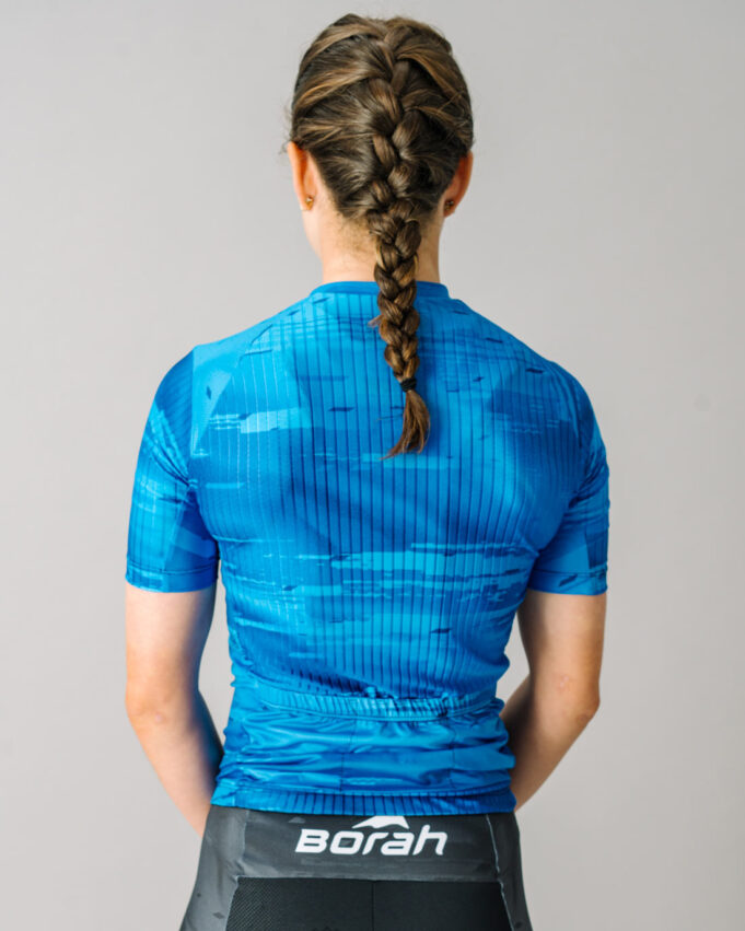 Back view of a female model wearing a blue custom Women's OTW Spark Cycling Jersey.