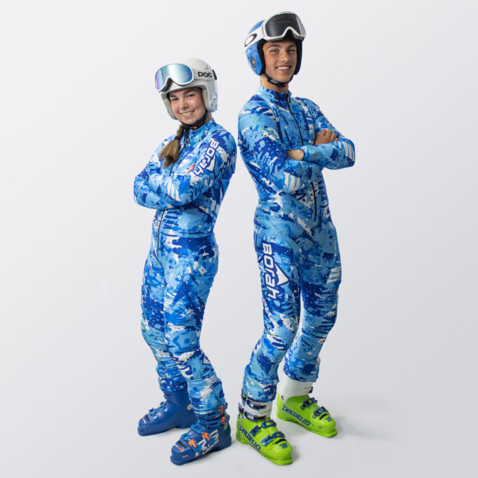 Two young athletes posing with their backs to one another wearing custom alpine race suits and gear.