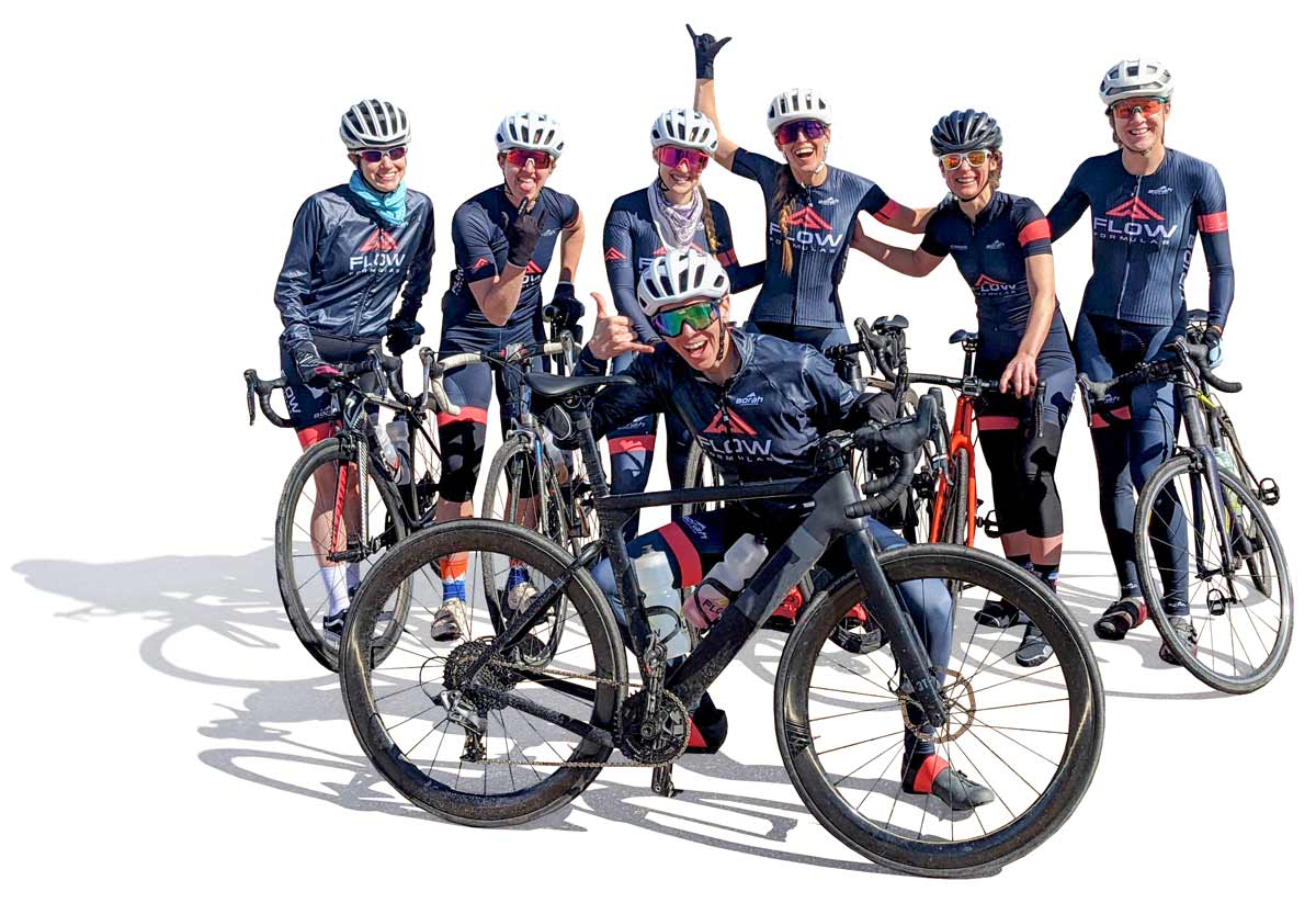 A team of women cyclists smiling and showing of their new custom cycling kits while posing next to their bikes.