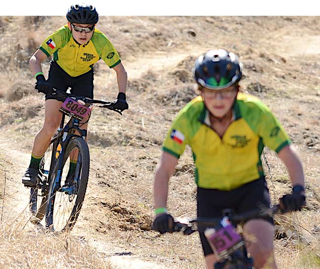 Two MTB riders biking on a dirt trail on a sunny day.