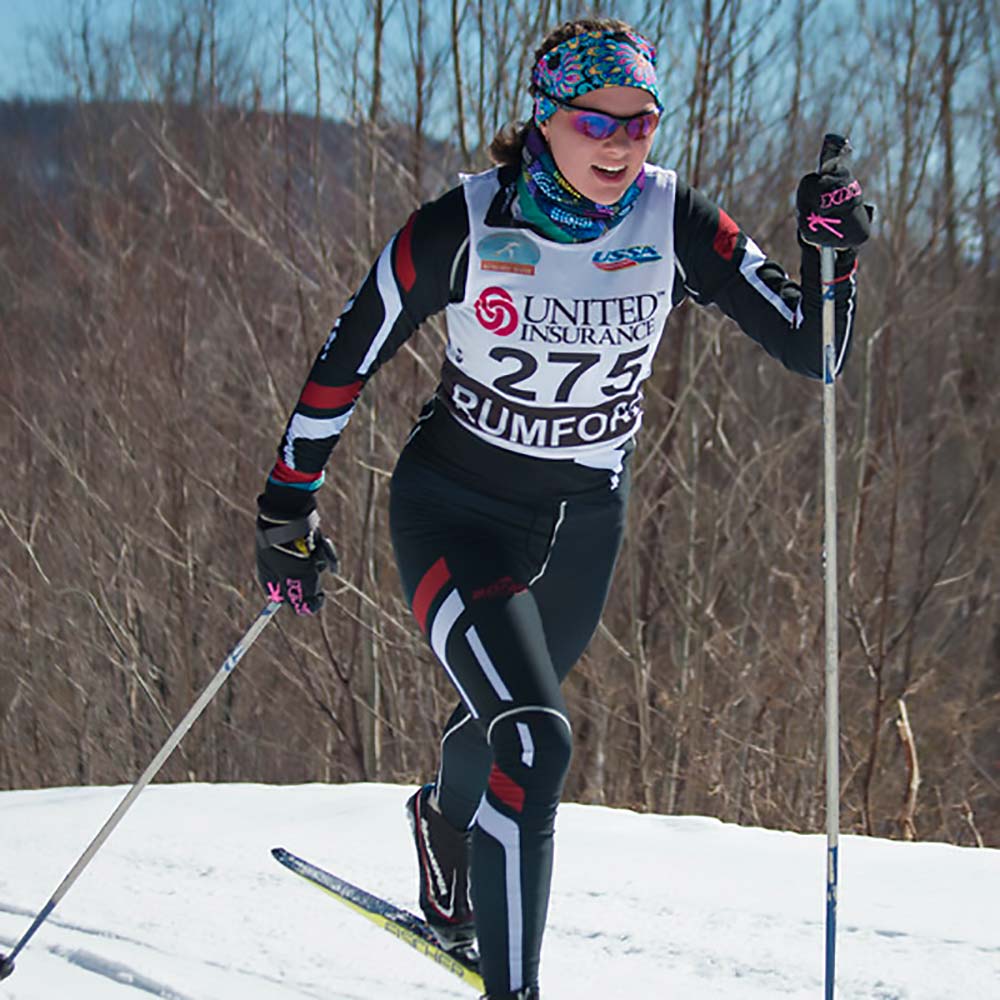 Female Nordic skier smiling in full stride.