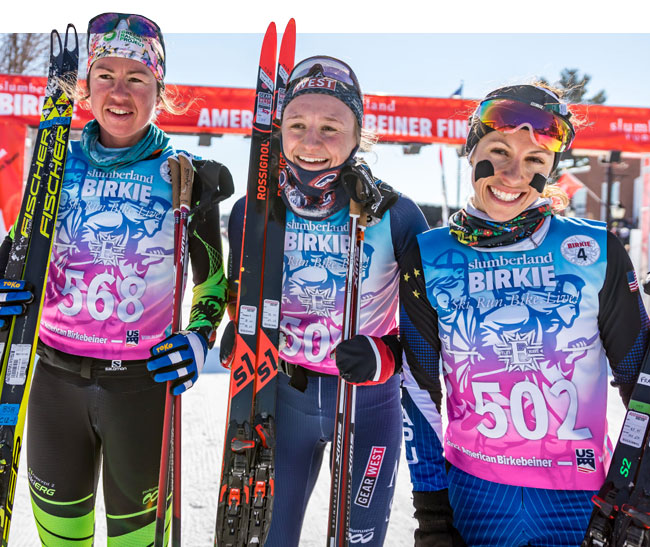 Three Nordic athletes smiling at the finish line wearing their iconic Birkie race bibs.