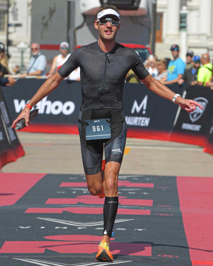 Triathlete crossing the finish line at an Ironman race wearing a prototype OTW Turbo Tri Skinsuit by Borah.