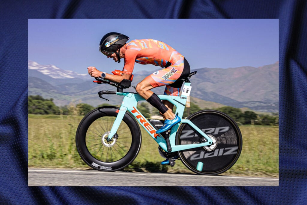 Triathlete riding a bicycle hard hunched over in the aero position position wearing a colorful custom cycling kit.