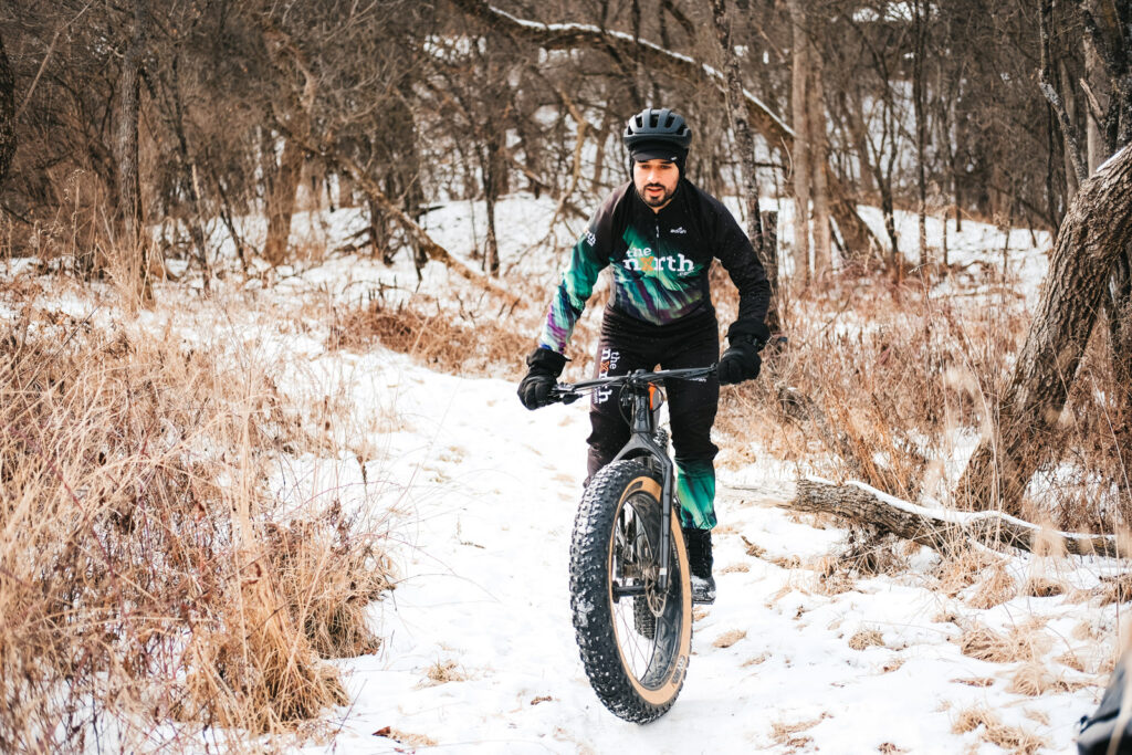 Winter cyclist riding on a snowy trail on a black fat bike wearing black Custom Borah Teamwear apparel.