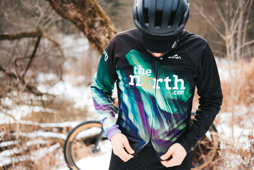 A cyclist looking down at the zipper on his custom OTW Thermal Cycling Jacket by Borah Teamwear. Woods and snow in the background.